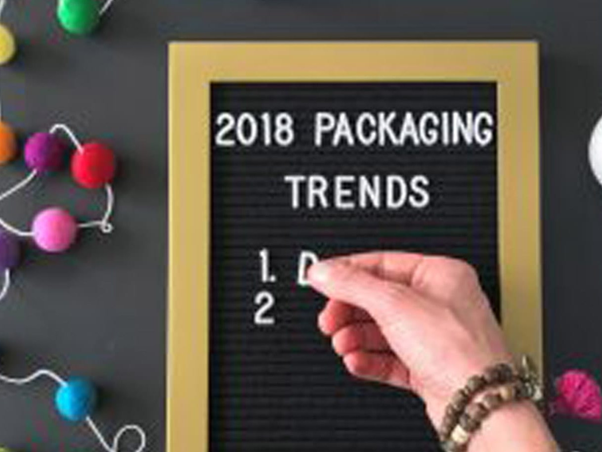 a woman's hand filling out a board that reads '2018 Packaging Trends'