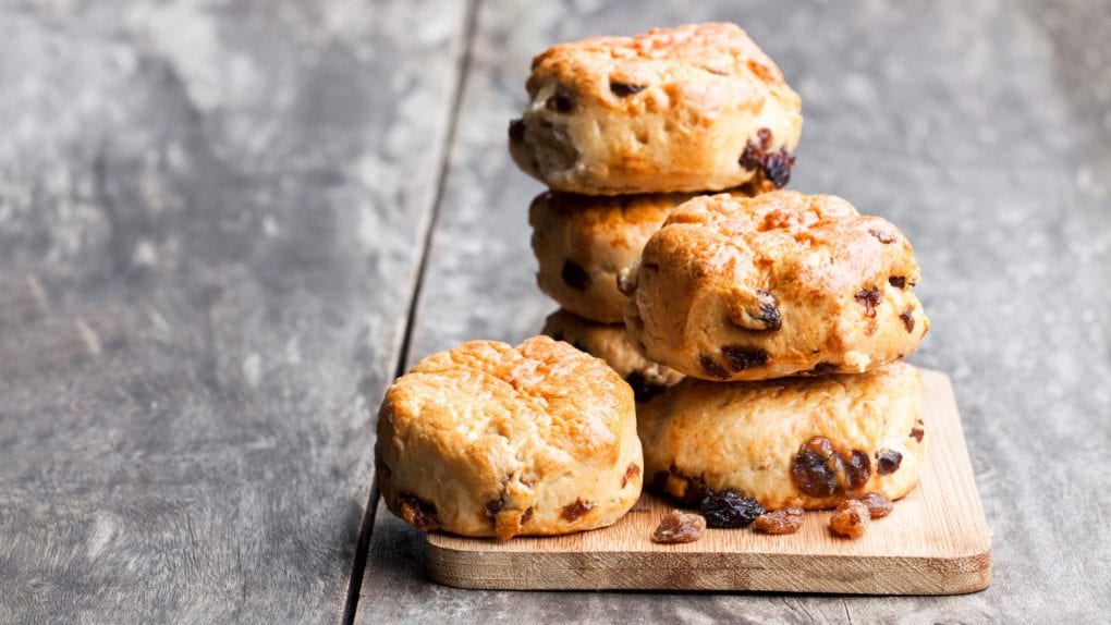 A photo of hearty scones, stacked on a wooden cutting board.